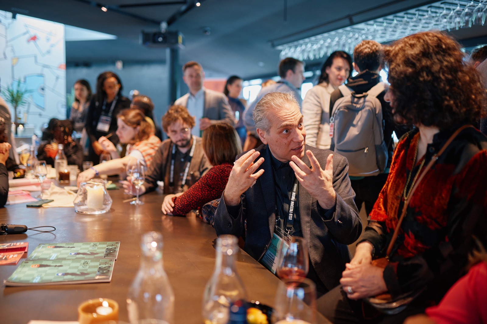 Attendees around the bar at a Sports & Dictators reception with The Signal materials on the table