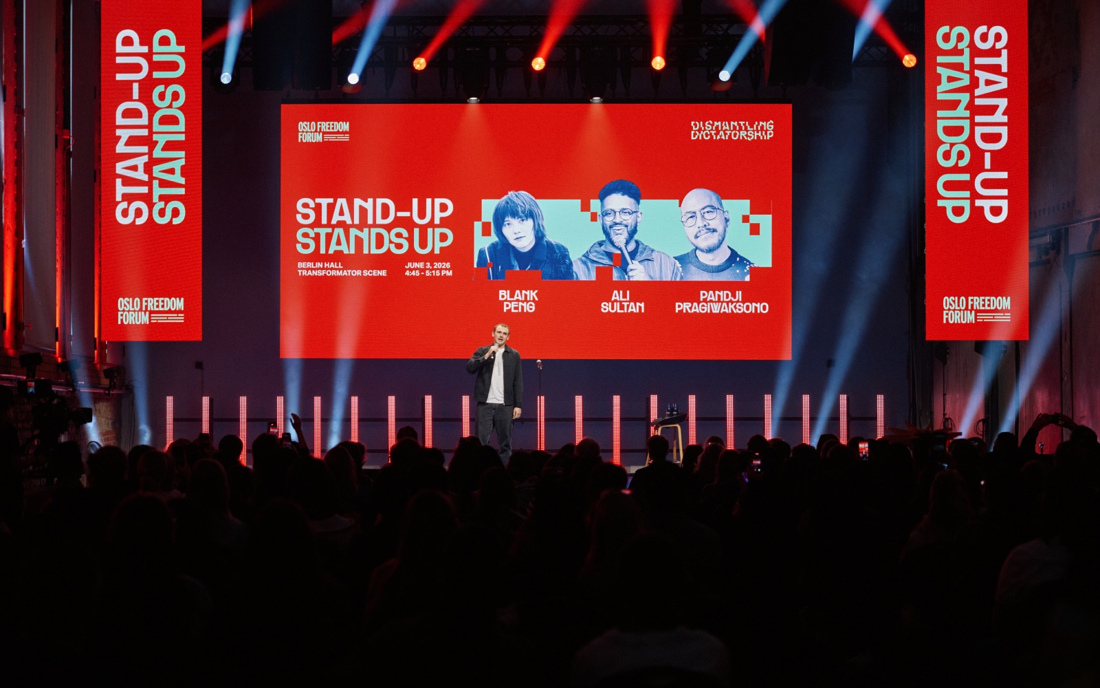 Stand-Up Stands Up on stage at the Oslo Freedom Forum with the show billboard behind